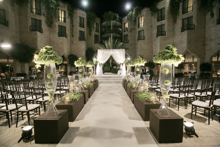 A courtyard set for an evening wedding reception with lights and flowers